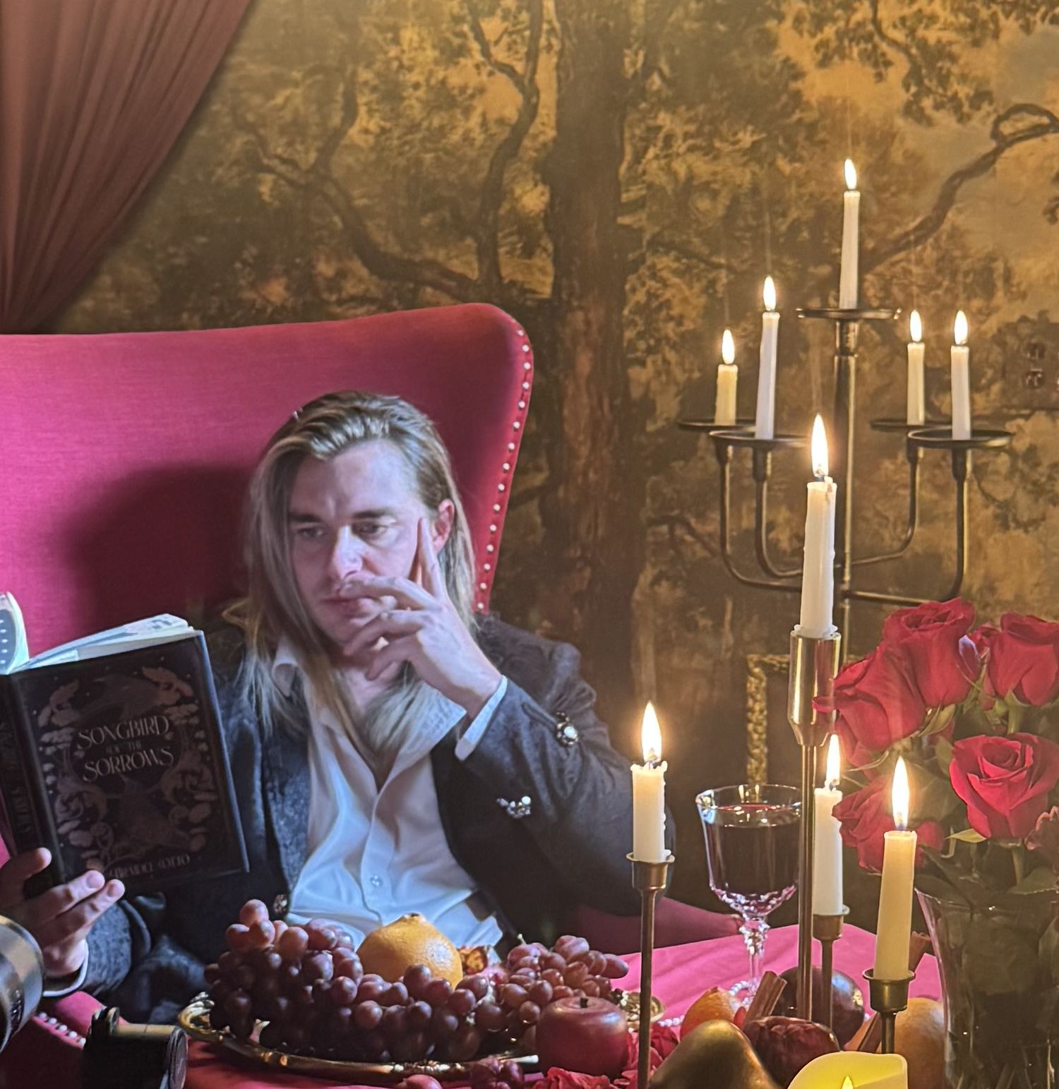 Jay Putty reading by candlelight in a red velvet chair